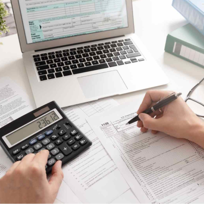 Someone fills out a tax form in front of a computer, with a calculator.