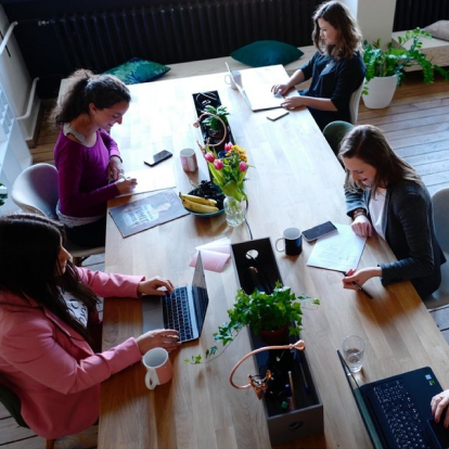 A group of women is shown collaborating and working around a long table.